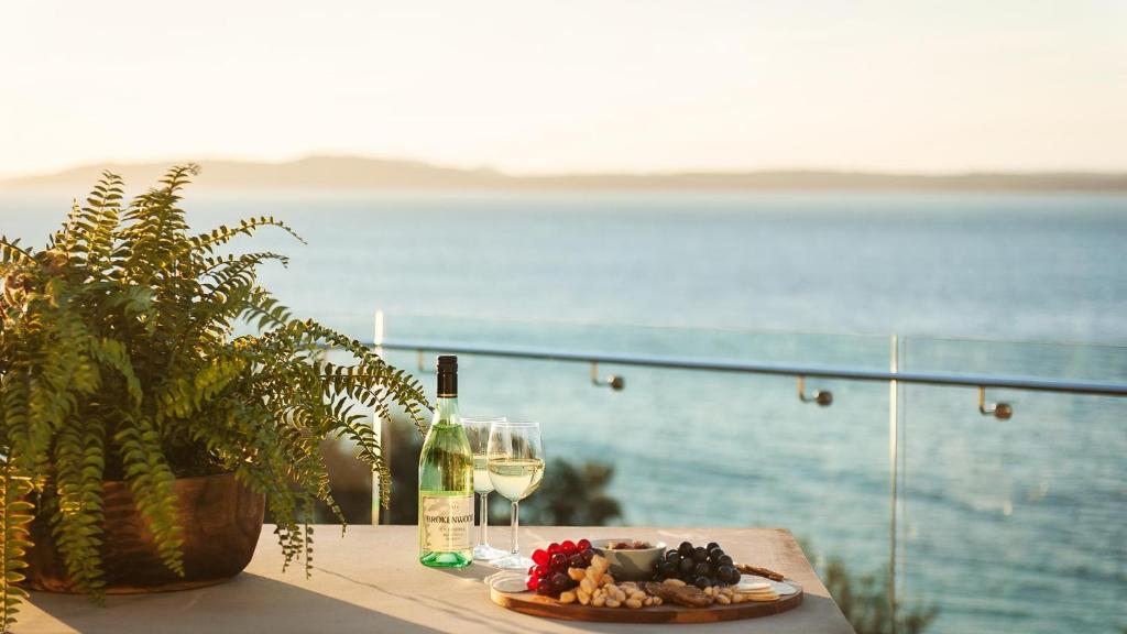 a table with a plate of food and a glass of wine at Riviera - Panoramic Water Views In The Heart Of Nelson Bay in Nelson Bay