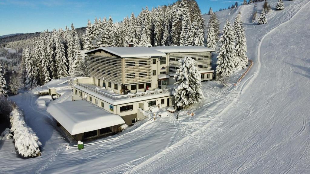 a large building on a snow covered slope with trees at Hotel Alpenrose Gerlitzen in Treffen