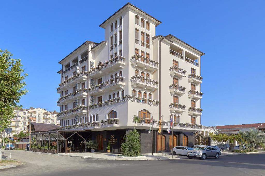 Un edificio alto y blanco con coches aparcados delante. en Garuda Boutique Hotel, en Sukhum
