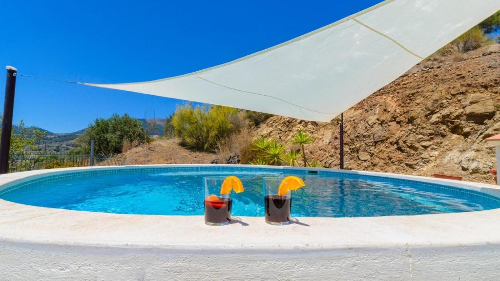 een zwembad met 2 stoelen en een parasol bij Casa del Pino Casarabonela by Ruralidays in Casarabonela
