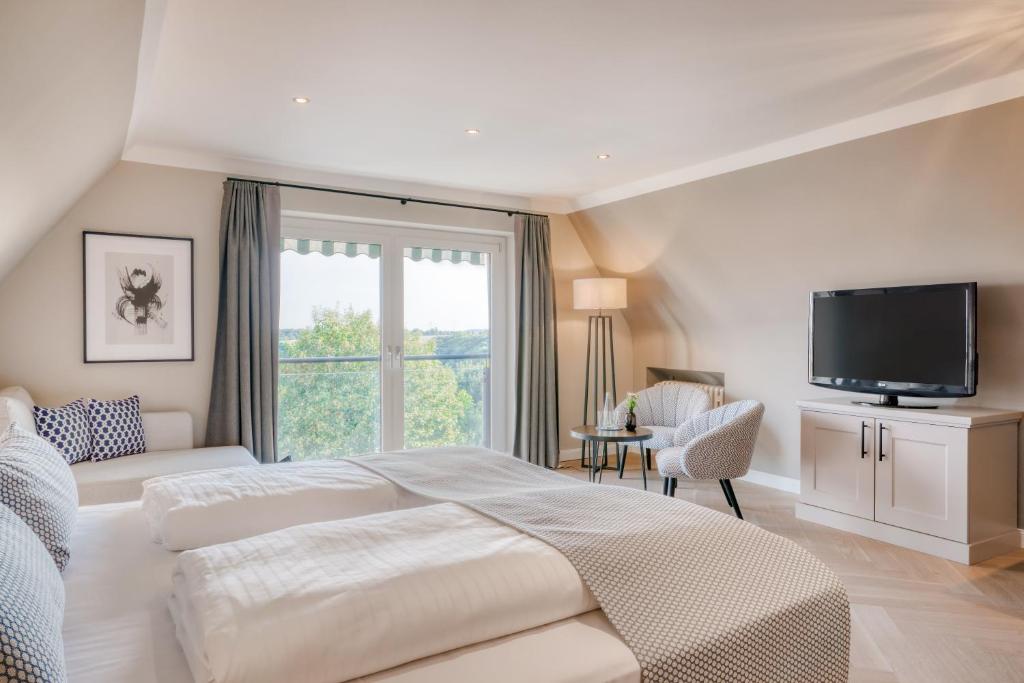 a white bedroom with a large bed and a television at Hotel Eisenhut in Rothenburg ob der Tauber