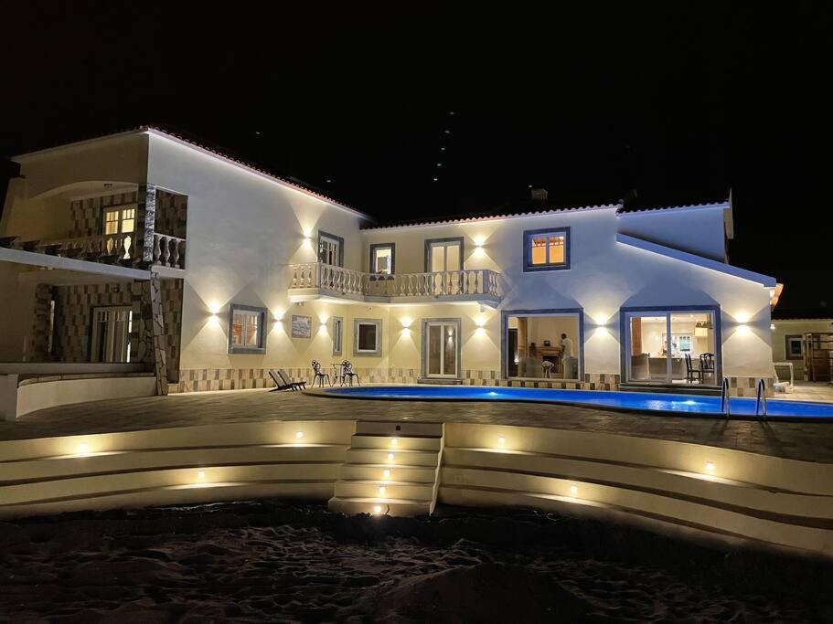 una gran casa blanca con piscina por la noche en Casa das Rosas en Carvoeira