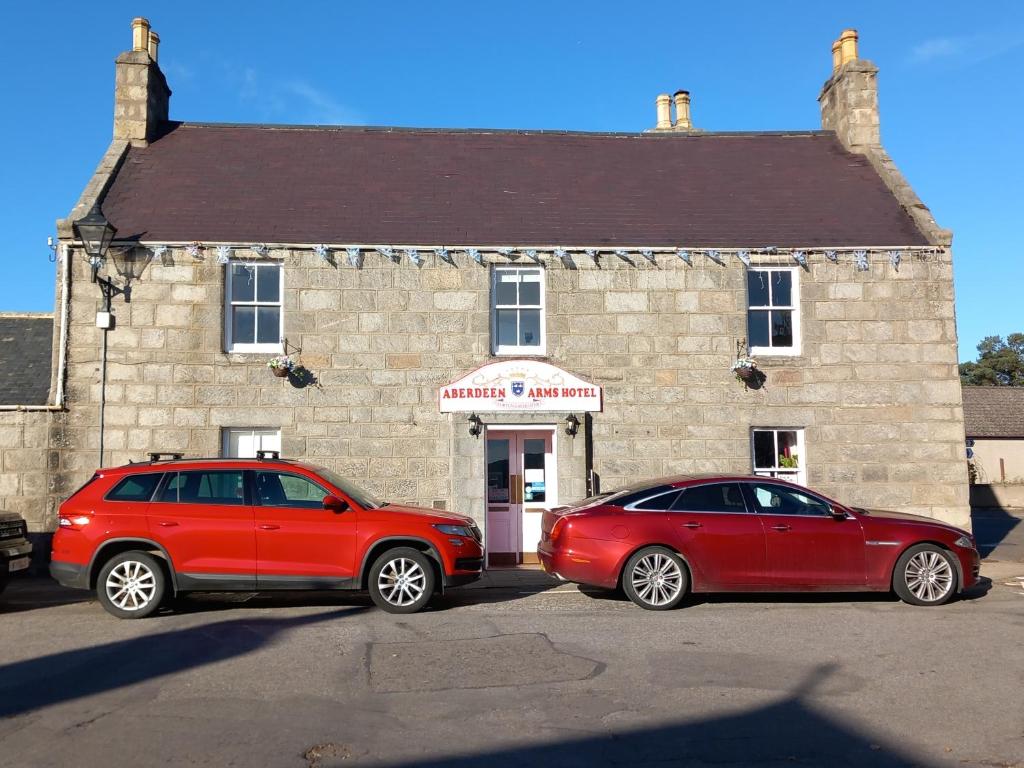 dwa czerwone samochody zaparkowane przed budynkiem w obiekcie Aberdeen Arms Hotel Tarland w mieście Tarland