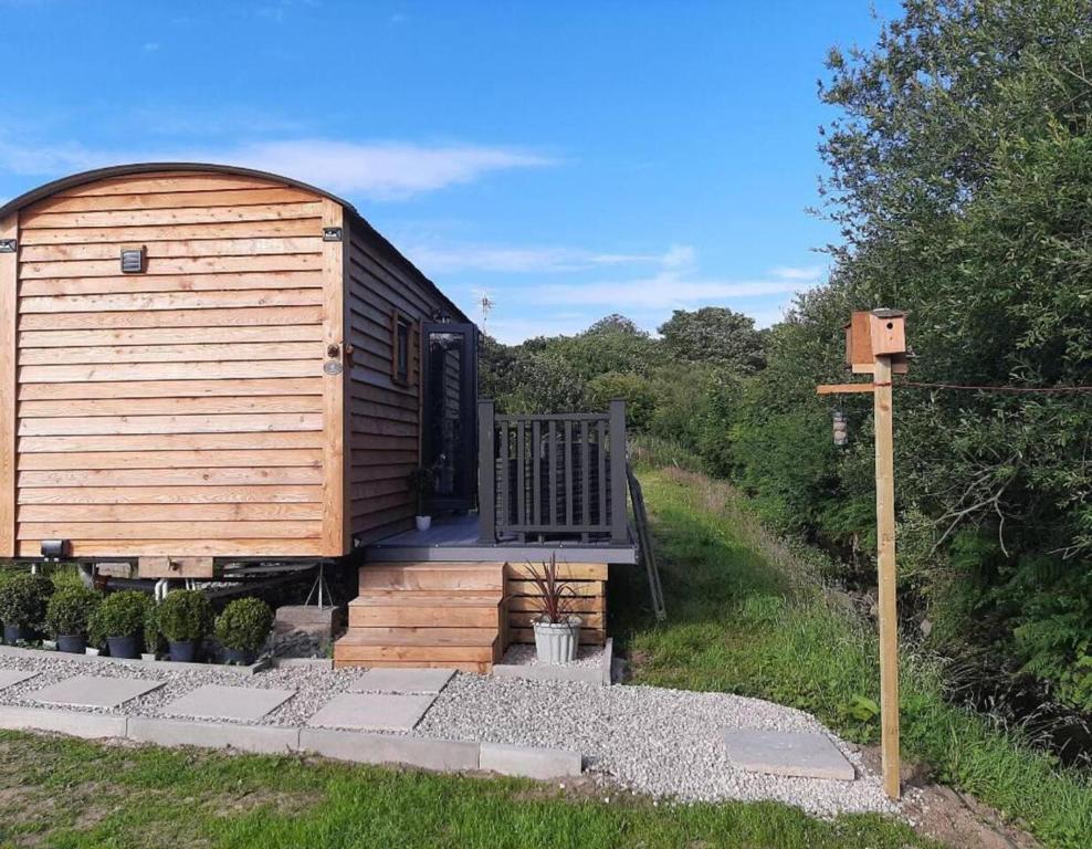 GwalchmaiにあるShepherds Hut with hot tub on Anglesey North Walesのポーチとデッキ付きの木造キャビン