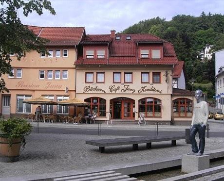 uma estátua de um homem sentado num banco em frente a um edifício em Pension Jung, Bäckerei-Konditorei & Café em Ruhla