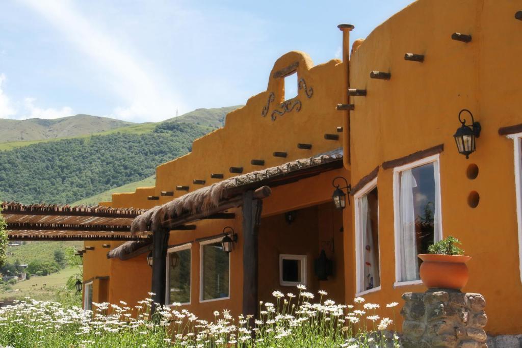 a building in the mountains with flowers in the foreground at Posada La Guadalupe in Tafí del Valle