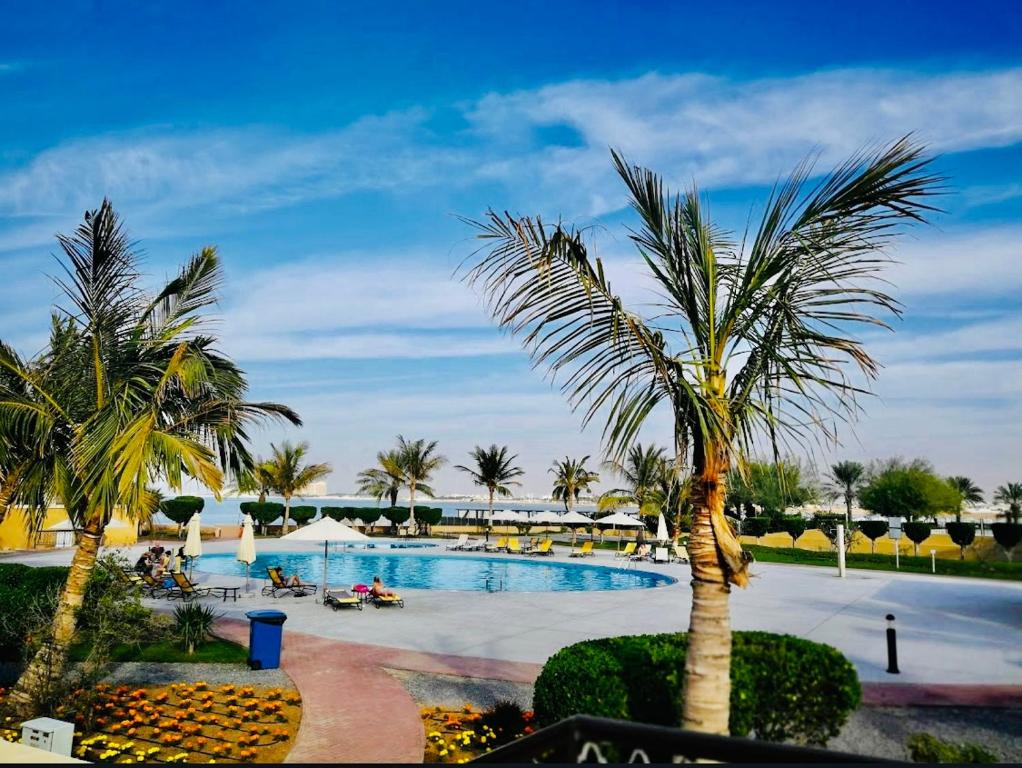 uitzicht op een zwembad met palmbomen bij Rixos Beach Apartment in Ras al Khaimah