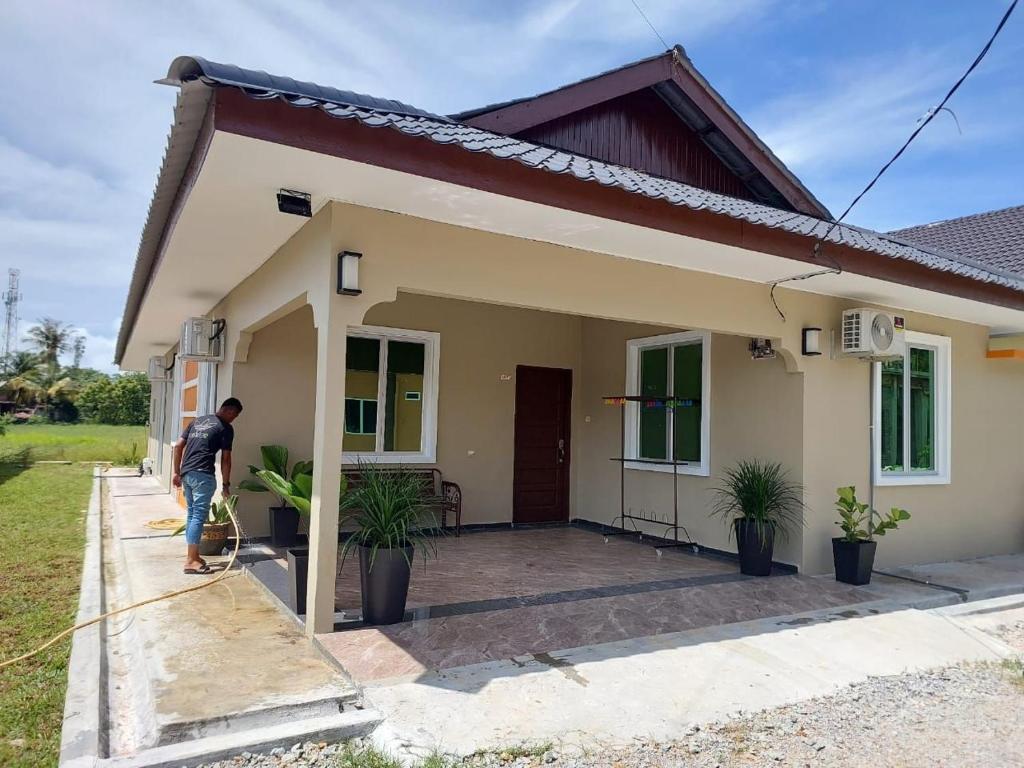 a man standing outside of a small house at NurHumaira Homestay in Pantai Cenang