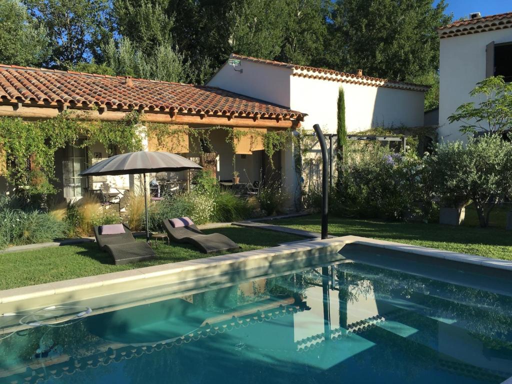 una piscina di fronte a una casa con ombrellone di Le Jardin de Lau ad Aubignan