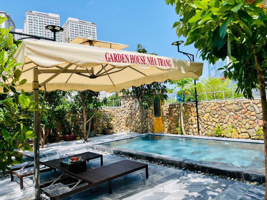 an umbrella over a swimming pool with a table and a bench at Garden House Nha Trang in Nha Trang