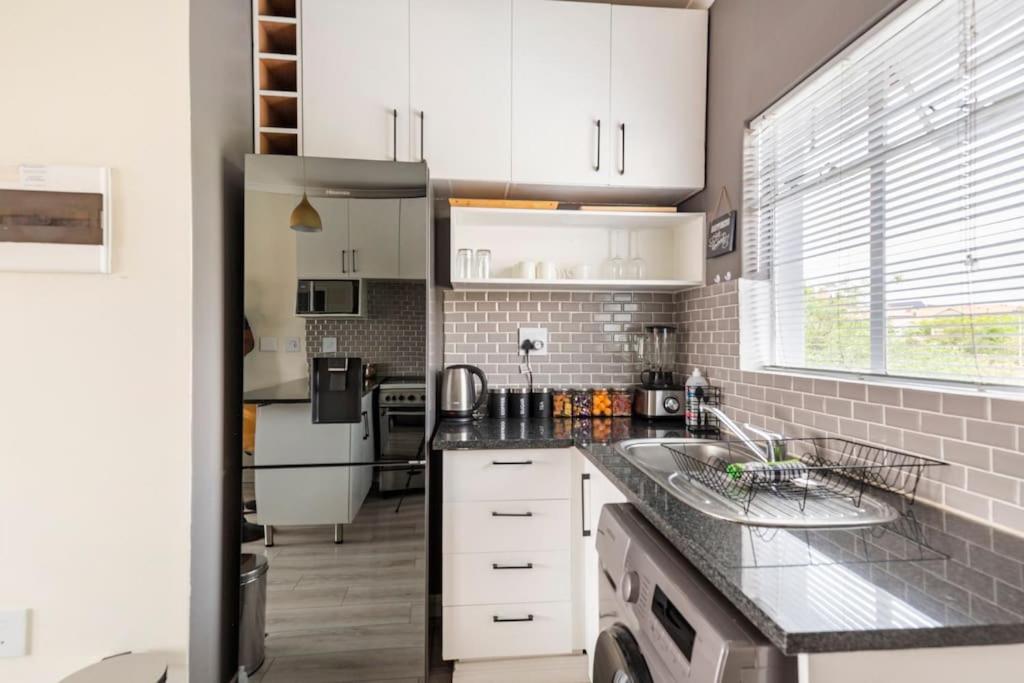 una cucina con armadi bianchi e piano di lavoro nero di Sunset View Apartment with Free Secure Parking in Central Location a Centurion