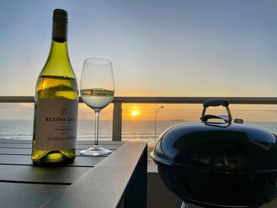 una botella de vino sentada en una mesa con una copa en Luxurious 2-bedroom beach apartment with a view! en Bloubergstrand
