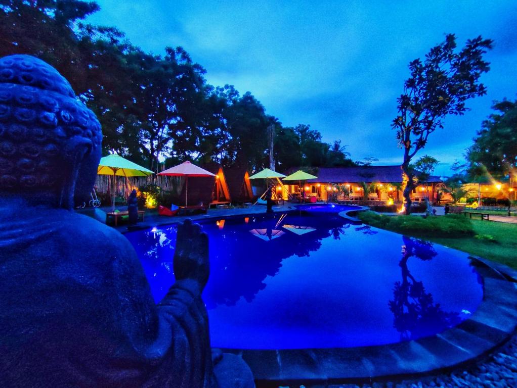 a statue sitting next to a swimming pool at night at Rich Farmer Eco House and Yoga in Pemuteran