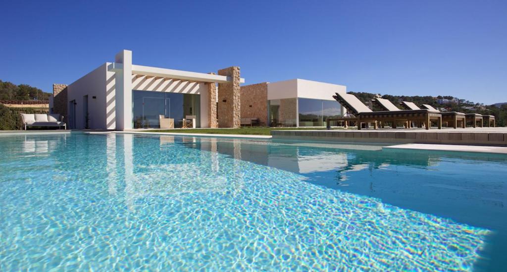 a swimming pool with blue water in front of a building at Contemporary Ibizan Villa Cala Conta Dream Short Walk to Beach San Jose in Cala Comte