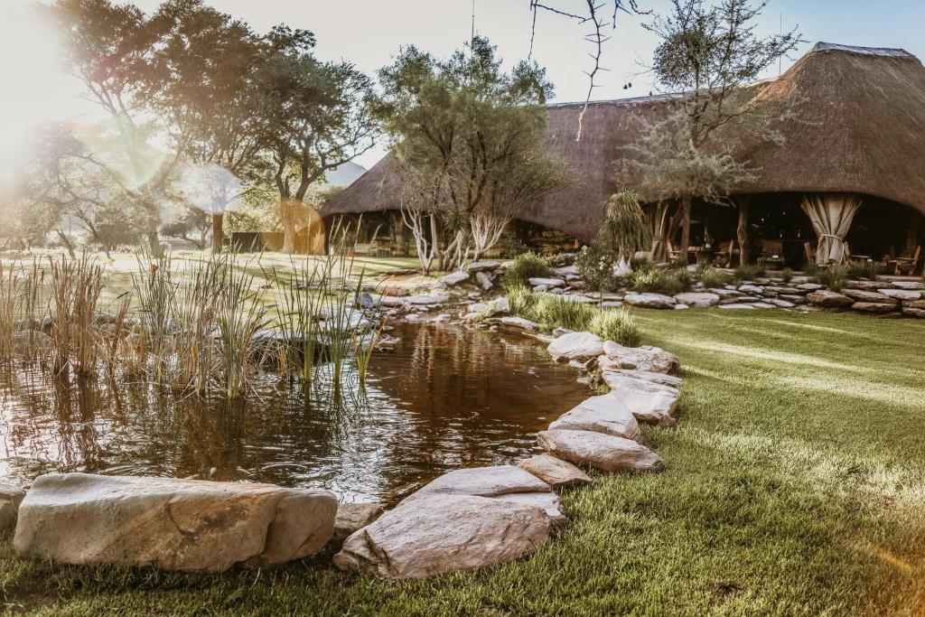 un jardín con un estanque y un edificio con techo de paja en Okapuka Safari Lodge, en Windhoek