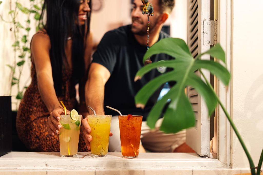 a man and a woman standing behind a table with four drinks at Discovery Hostel in Rio de Janeiro