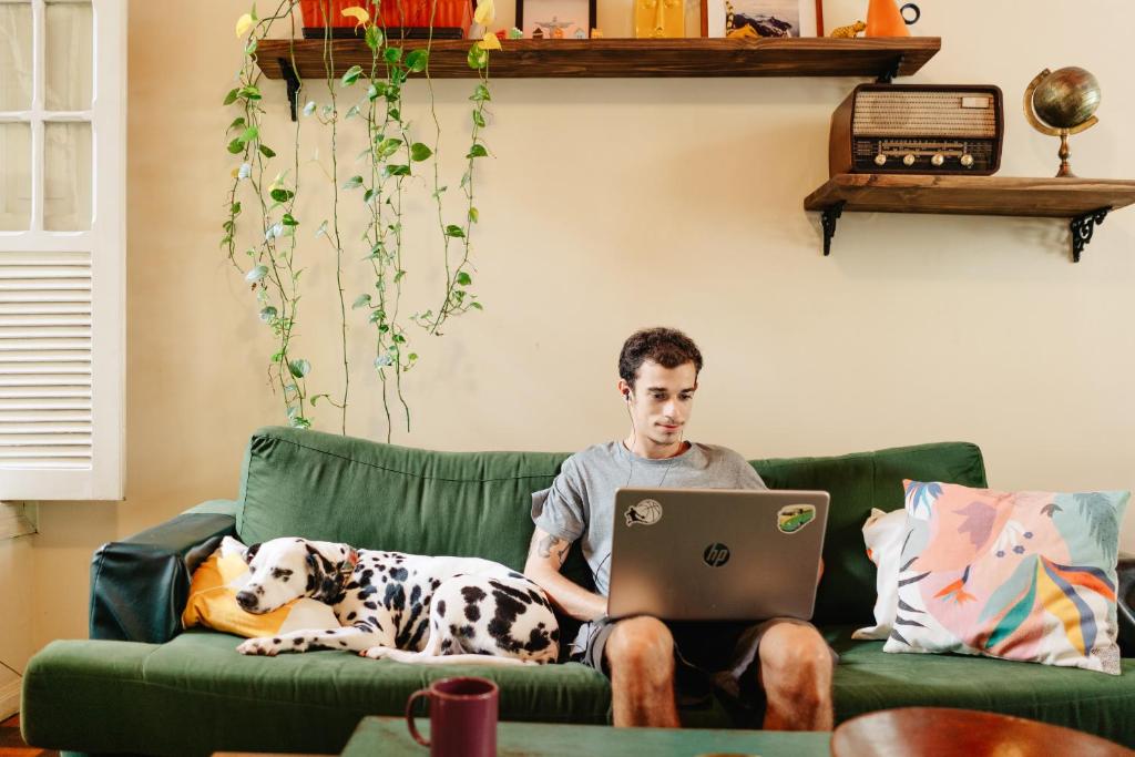 a man sitting on a couch with a dog and a laptop at Discovery Hostel in Rio de Janeiro