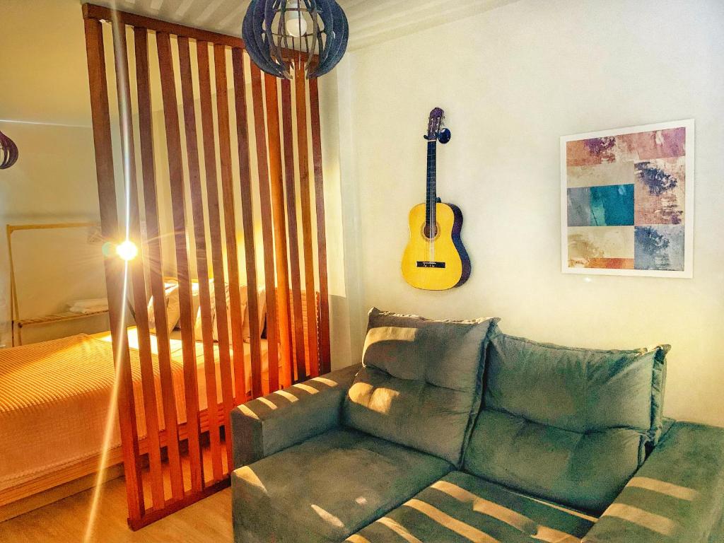 uma sala de estar com um sofá e uma guitarra na parede em LOFT aconchegante no Centro de Macaé, Wifi, Ar condicionado e Cozinha completa em Macaé