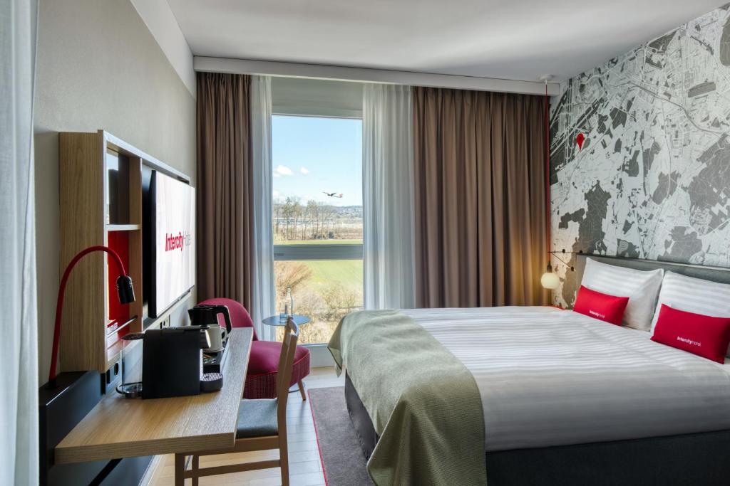 una camera d'albergo con letto, scrivania e finestra di IntercityHotel Zürich Airport a Rümlang