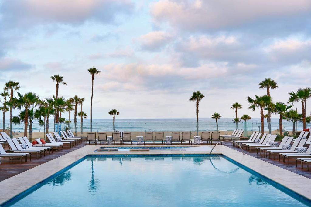 una piscina en la playa con sillas y palmeras en Paséa Hotel & Spa en Huntington Beach