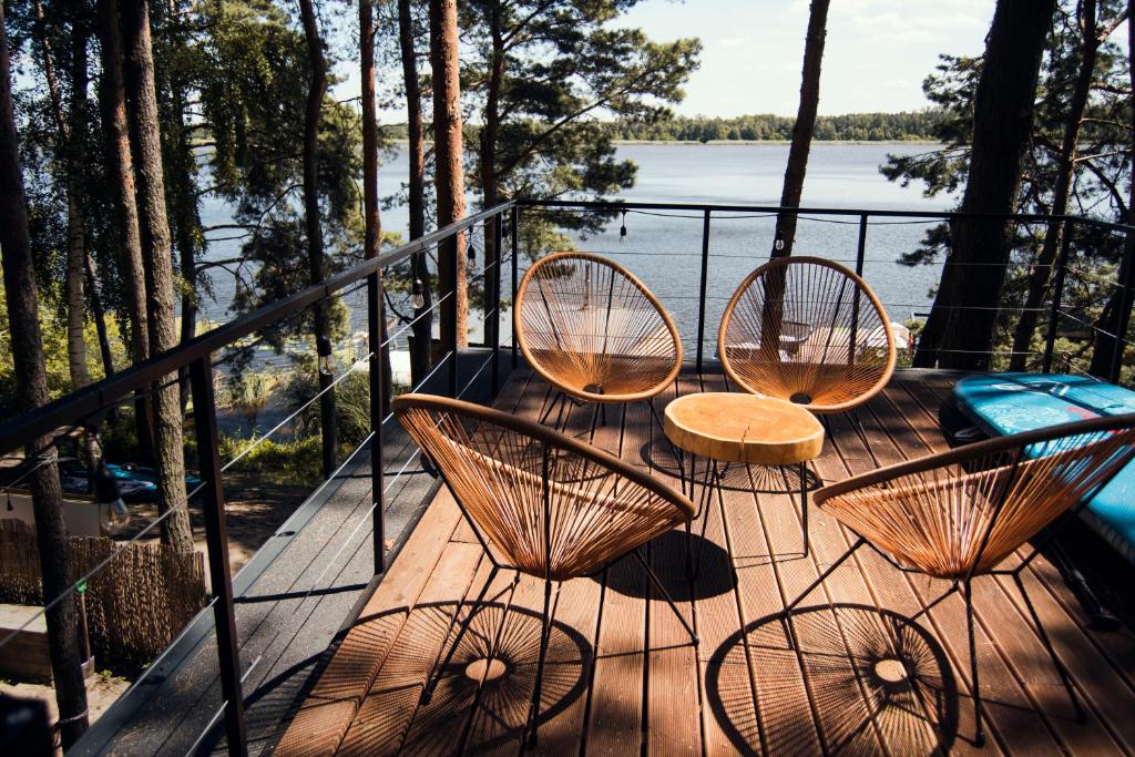 three chairs and a table on a deck with a view of the water at Nad Narvią - dom na drzewie in Serock