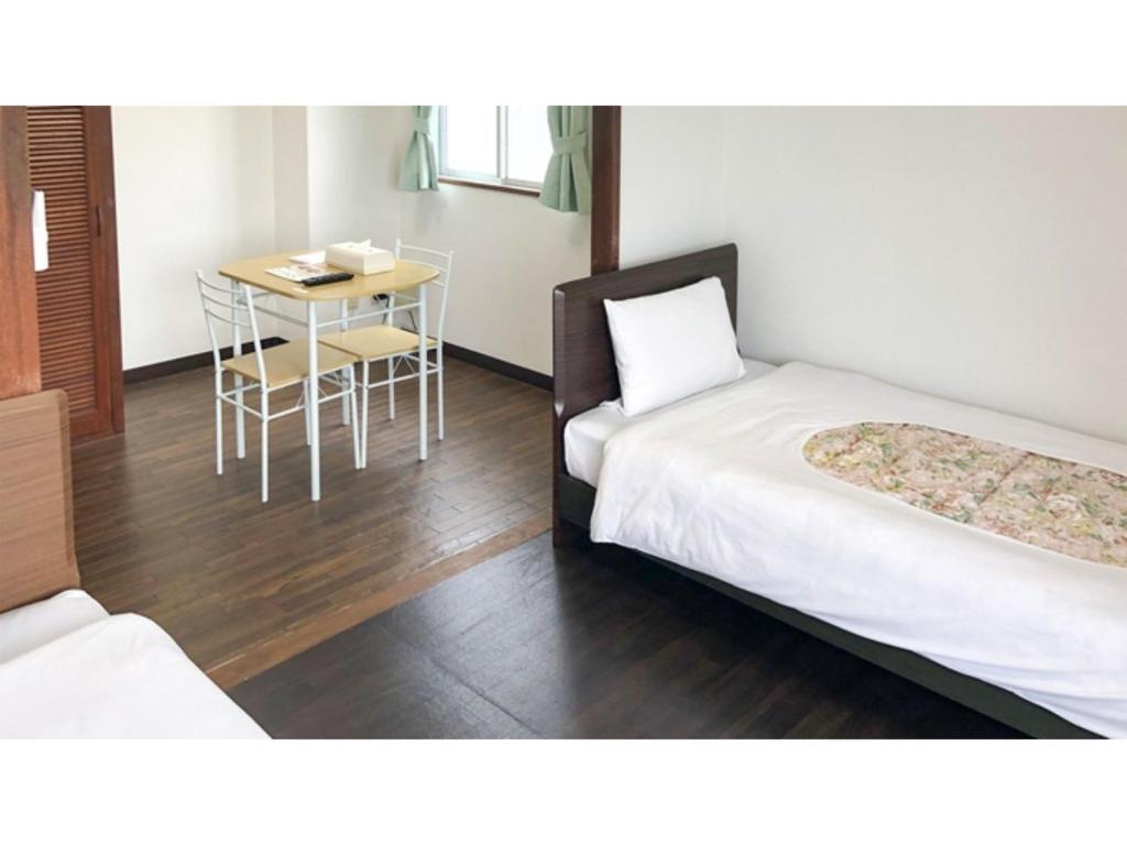 Cette chambre comprend deux lits et une table avec une chaise. dans l'établissement Sunset Hills Inn Naha - Vacation STAY 77494v, à Naha