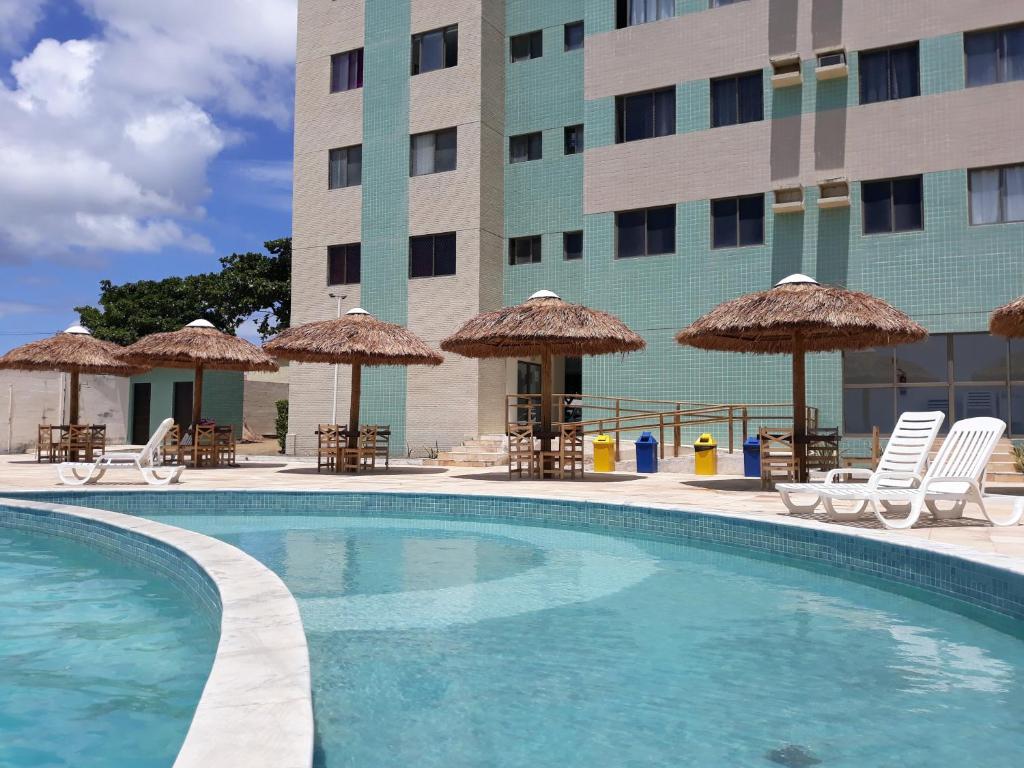 una piscina di fronte a un hotel con sedie e ombrelloni di Apartamento com 2 quartos de FRENTE PARA O MAR a Maceió