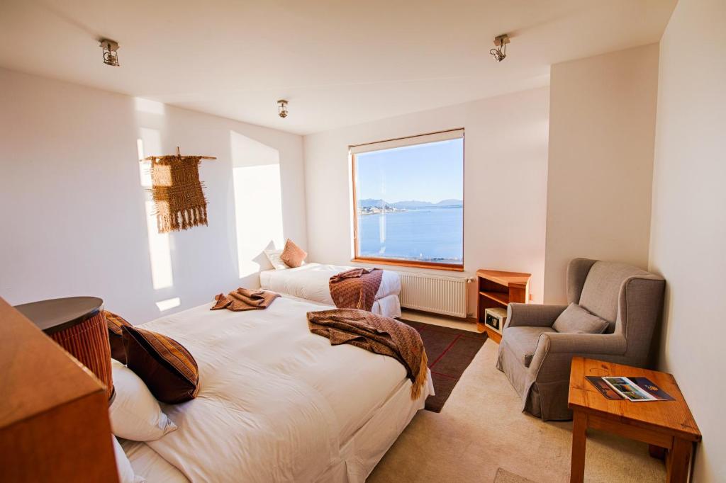 a bedroom with a bed and a chair and a window at Weskar Lodge Hotel in Puerto Natales