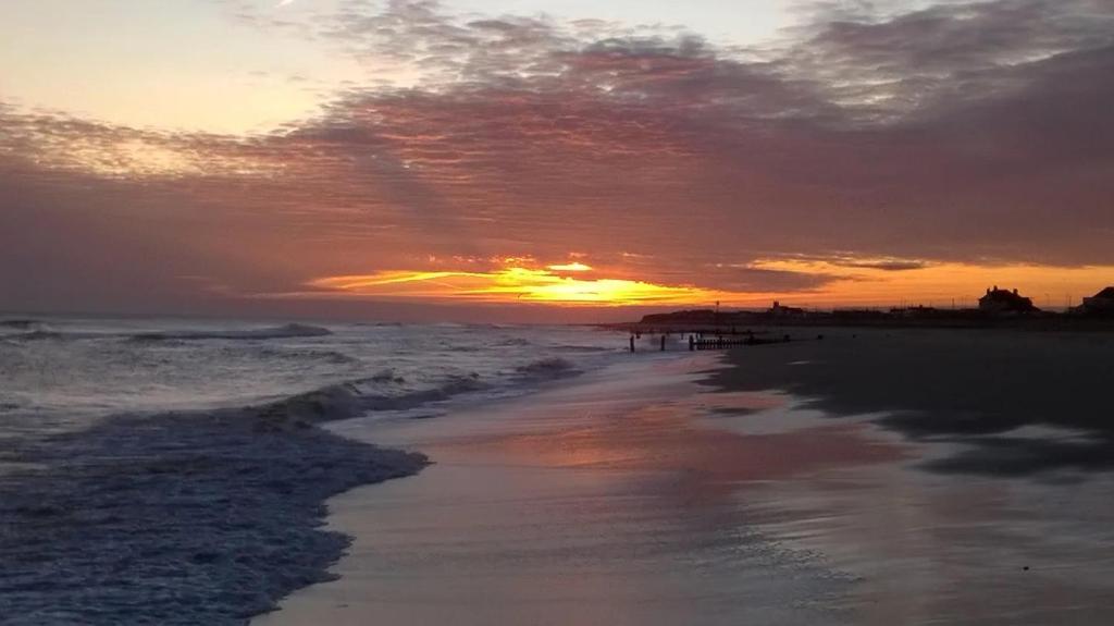 einen Sonnenuntergang am Strand mit dem Meer in der Unterkunft Sundial Cottage in Norwich