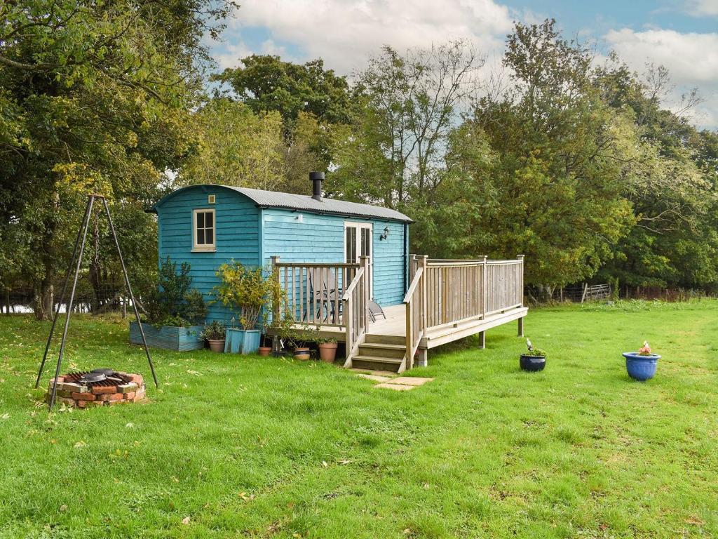 een blauw tiny house in een tuin met een veranda bij The Shepherds Hut in Herstmonceux