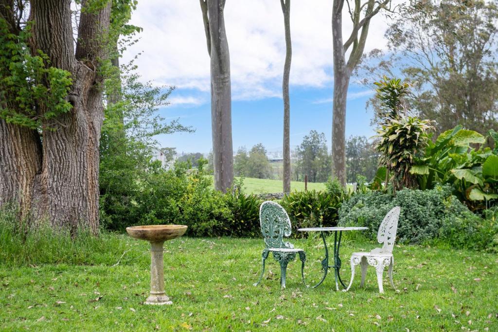 2 Stühle, ein Tisch und ein Vogelbad im Gras in der Unterkunft Tatbern Park Cottage Wallalong in Wallalong