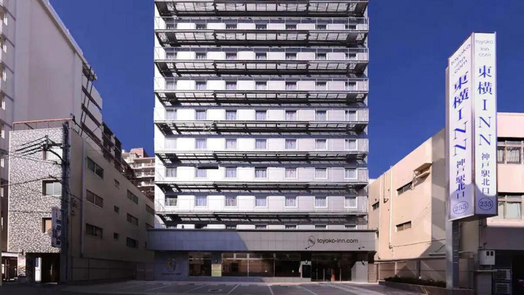 um edifício alto e branco com uma placa à frente. em Toyoko Inn JR Kobe eki Kita guchi em Kobe