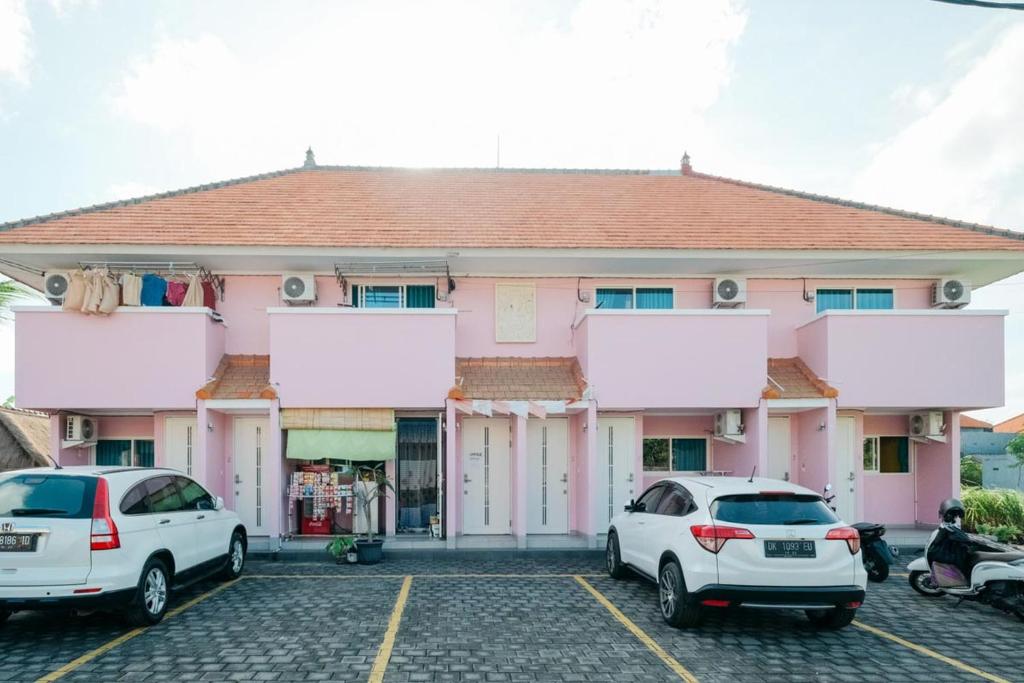 dos autos estacionados en un estacionamiento frente a un edificio rosa en RedDoorz at Kawaii Apartment Jimbaran, en Balian