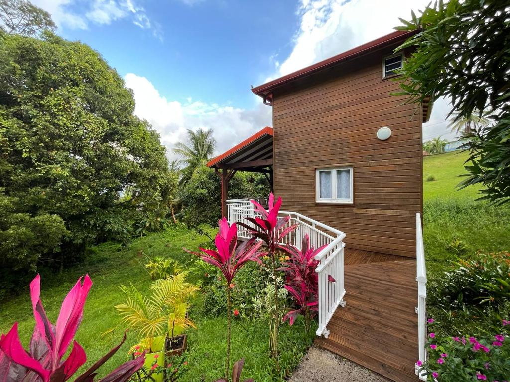 une maison avec une terrasse couverte et des fleurs devant elle dans l'établissement Mahogany Lodge - Oasis cosy, à Rivière-Pilote
