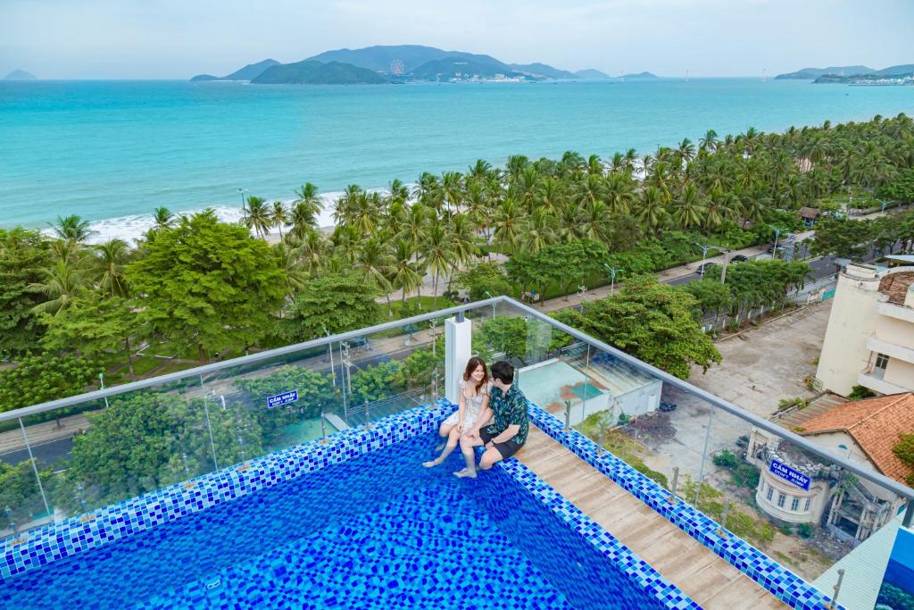 a couple sitting on the edge of a swimming pool overlooking the ocean at Azura Gold Hotel & Apartment in Nha Trang