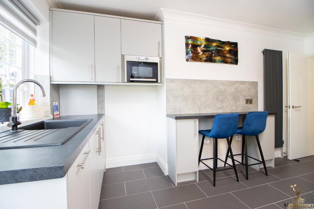 una cocina con armarios blancos y taburetes azules en Station Lodge close to City Centre with parking en Exeter