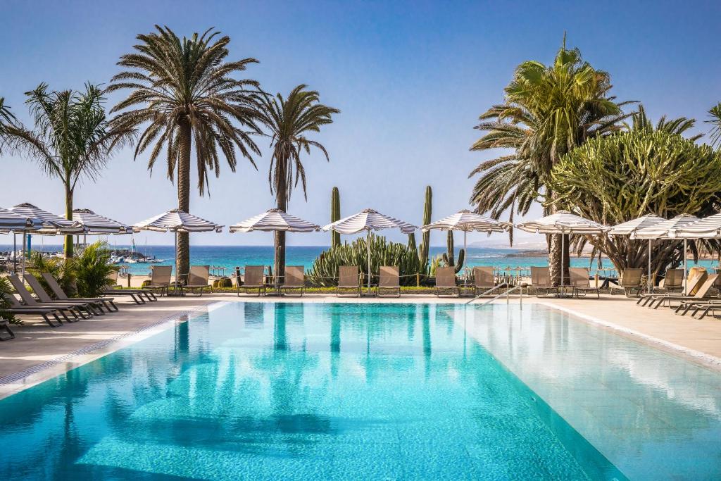 una piscina con palmeras y sombrillas en Barceló Fuerteventura Royal Level - Adults Only en Caleta de Fuste