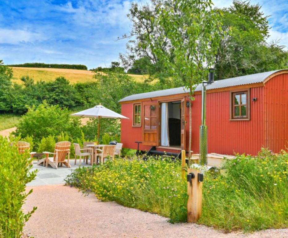 a red tiny house with a table and an umbrella at Finest Retreats - Willow Luxury Shepherds Hut in Dittisham
