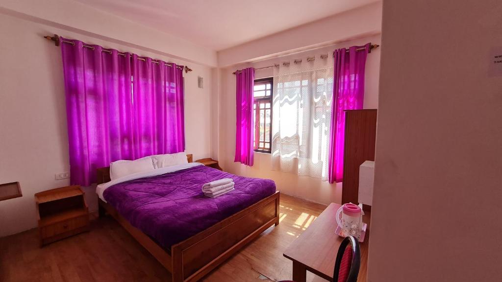 - une chambre avec des rideaux roses et un lit avec des draps violets dans l'établissement Hotel Himsagar, à Pemayangtse