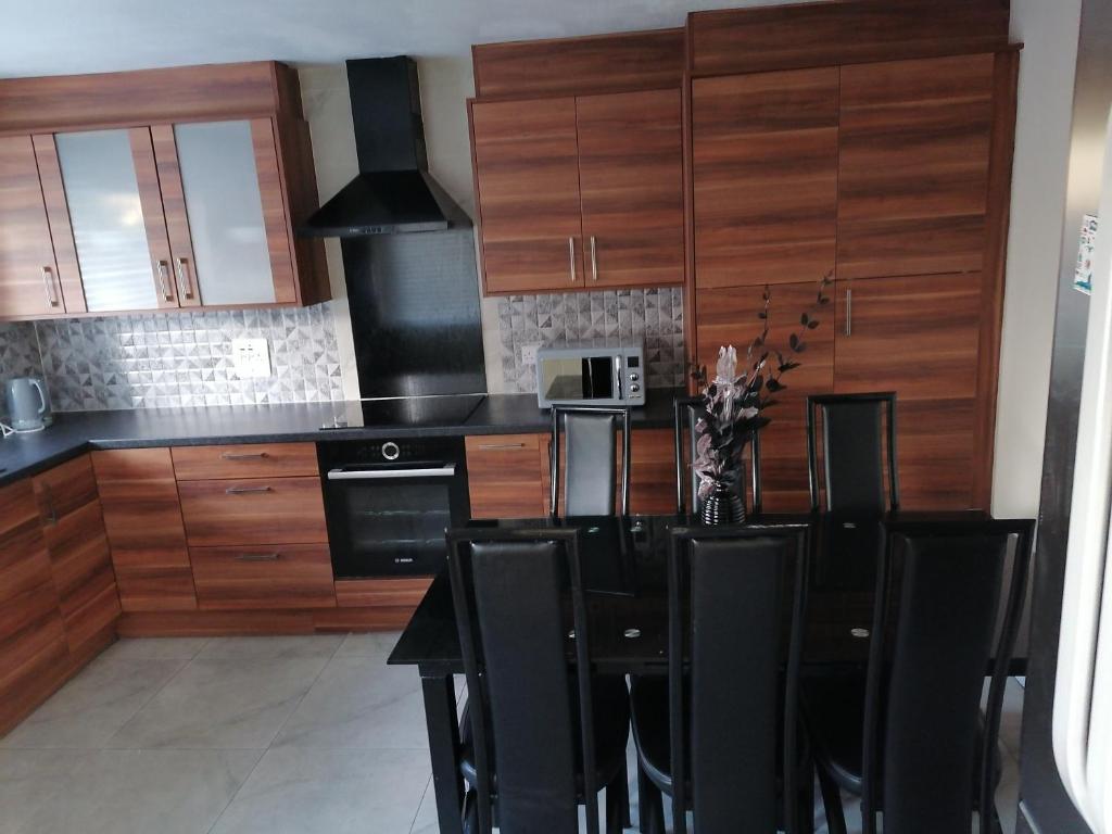 una cocina con armarios de madera, mesa negra y sillas en Large House with 3 Bedrooms house, 5 guests near city/Manu stadiums, en Mánchester