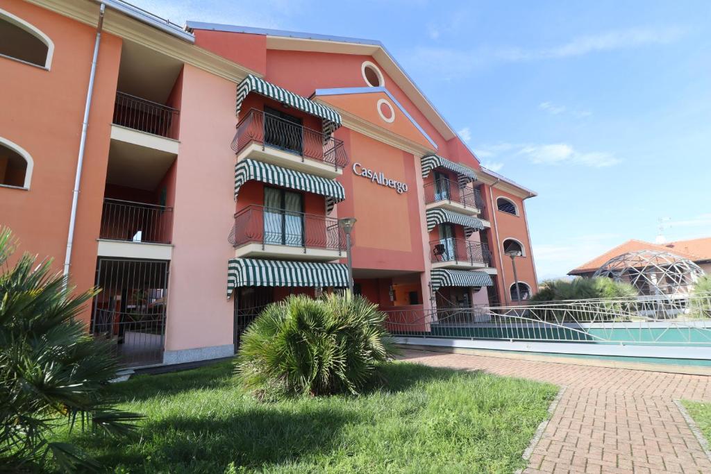 różowy budynek z basenem przed nim w obiekcie CasAlbergo - Superior Lake Apartments w mieście Castelletto sopra Ticino