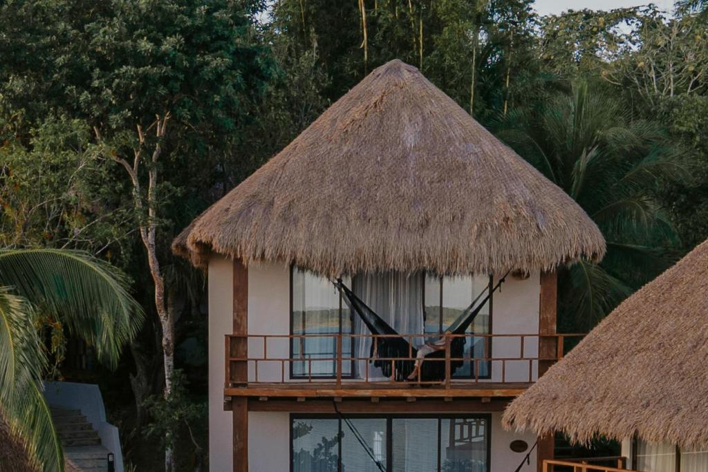 una casa con techo de paja y una persona sentada en un balcón en Khaban Bacalar Hotel Boutique, en Bacalar