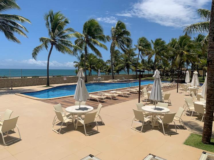 um grupo de mesas e cadeiras com guarda-sóis ao lado de uma piscina em Itacimirim vilage Villas da Praia em Itacimirim