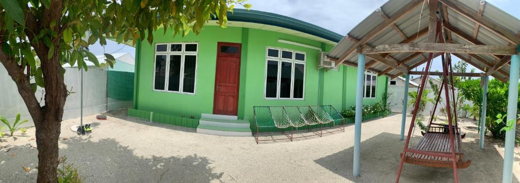 a green building with a red door and a swing at Arrow in Vashafaru