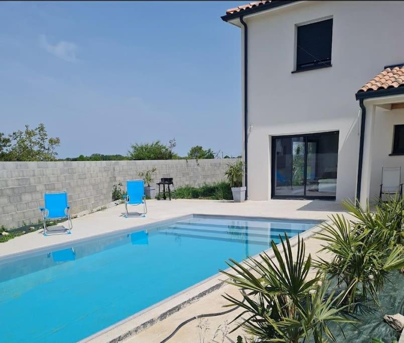 uma piscina com duas cadeiras azuis e uma casa em magnifique villa avec piscine et spa em Merville