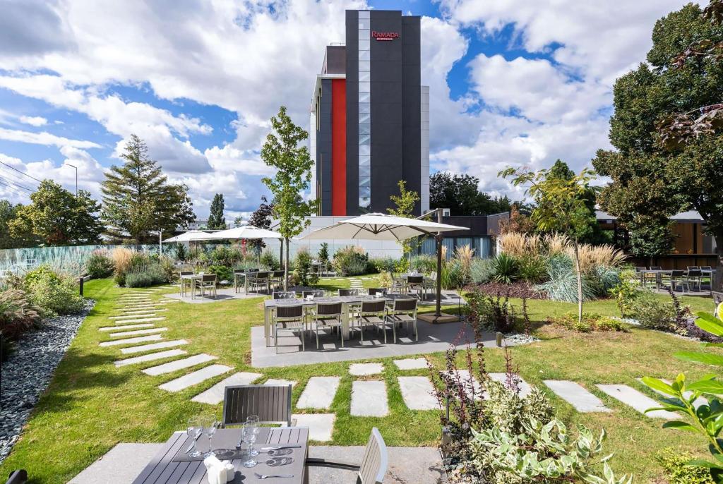 um jardim com mesas e cadeiras e um edifício alto em Ramada by Wyndham Slatina Parc em Slatina