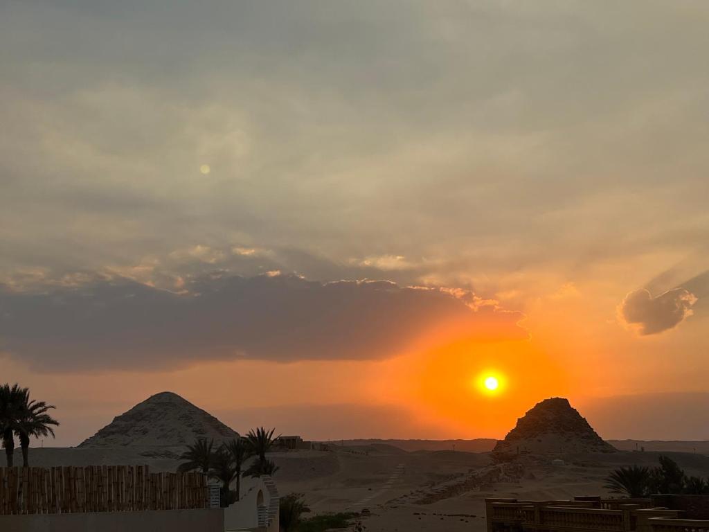 a sunset in the desert with mountains and palm trees at Sunset Guesthouse Abusir in Cairo