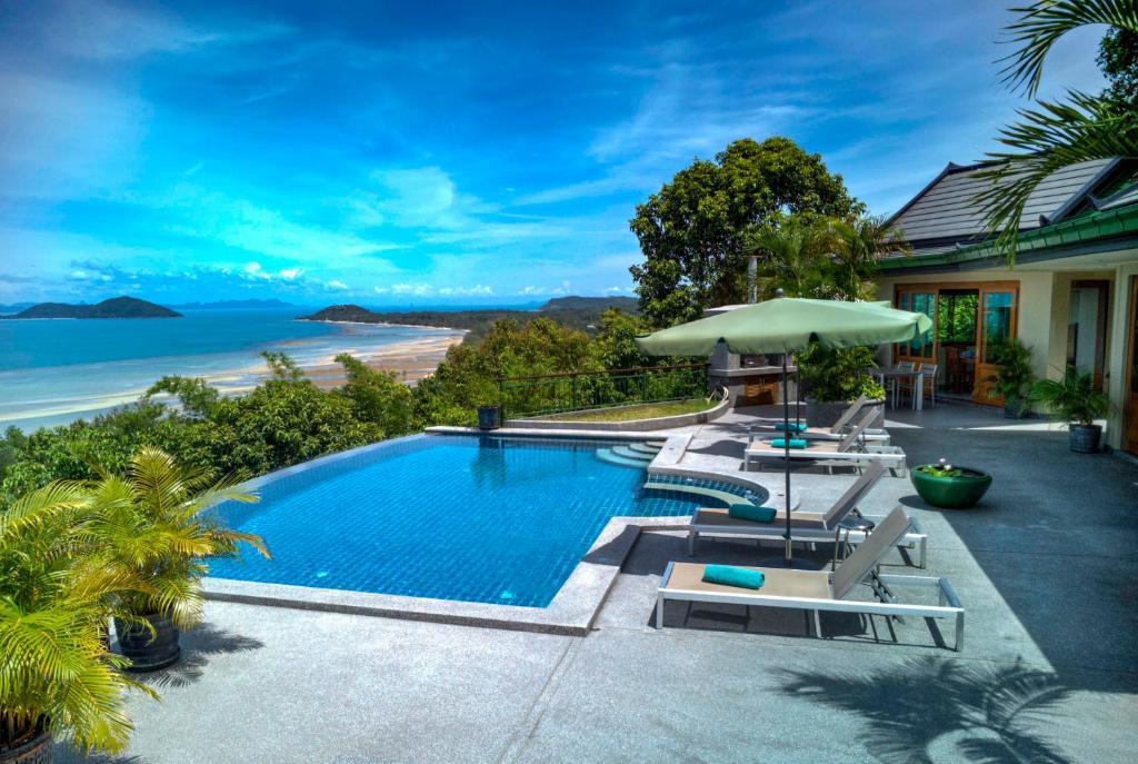 a swimming pool with chairs and an umbrella and the ocean at Villa Moonstone in Laem Set Beach