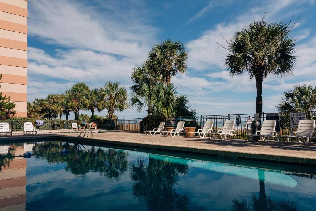 a swimming pool with lounge chairs and palm trees at Sandcastle Oceanfront Resort at the Pavilion in Myrtle Beach