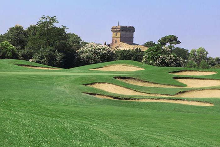 a green golf course with a tower in the background at Ameno house in Casale SantʼAntonio